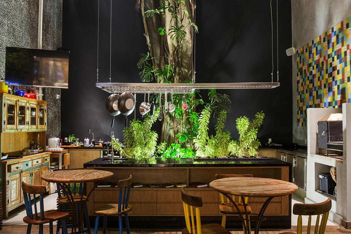 A biophilic kitchen space with indoor plants and a tree surrounded by the operating space of the kitchen, counters, and cabinets.