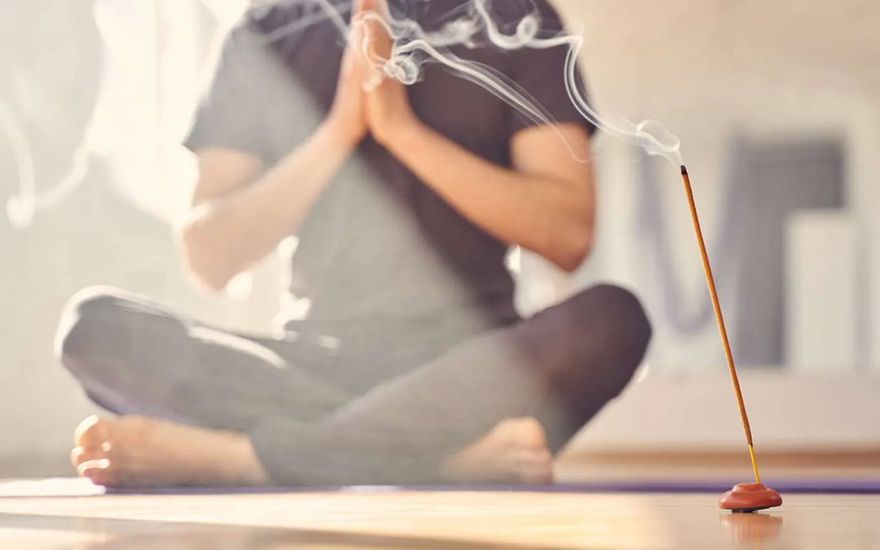 A photo of a person meditating with an incense sticK, a good example of having aromatherapy and meditation together.